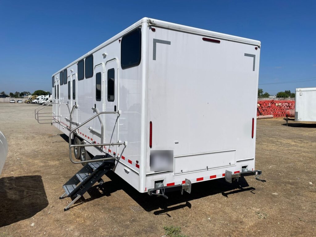 12-station bunkhouse sleeper trailer with bunk windows and fold-down steps in a gravel staging yard, The Lavatory Los Angeles