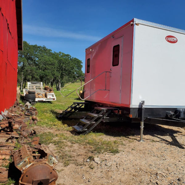 Bathroom trailer with steps set on a dirt ranch lot next to a barn, The Lavatory Los Angeles
