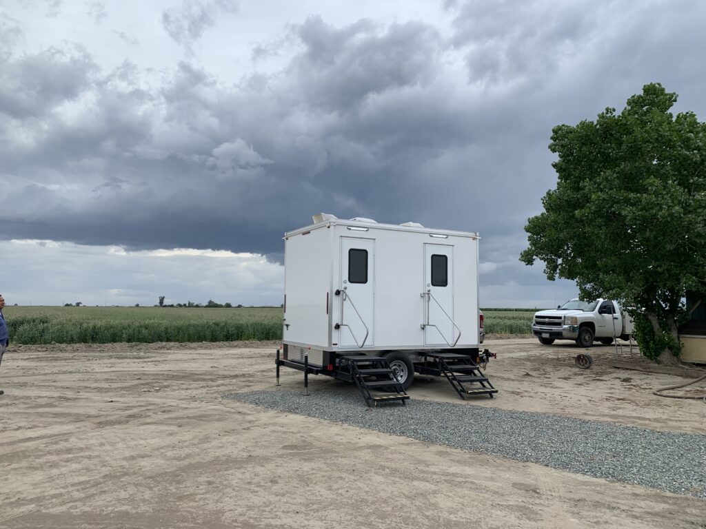 Bathroom trailer on a gravel pad at a farm field under storm clouds, The Lavatory Los Angeles