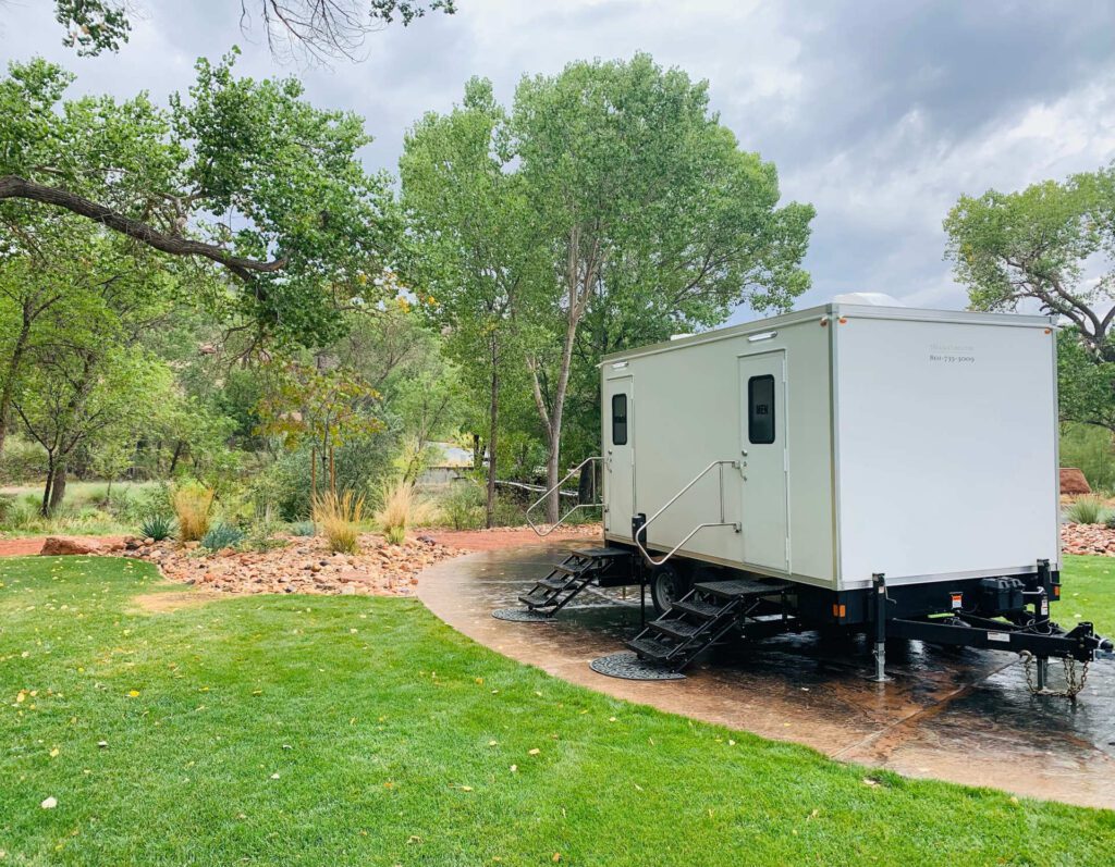 Mobile bathroom trailer parked on a curved path beside a green lawn and garden, The Lavatory Los Angeles