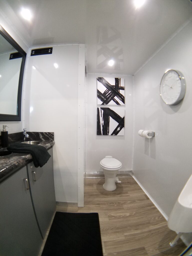 Granite vanity, toilet and black and white wall art inside a 2-station bathroom trailer, The Lavatory Los Angeles