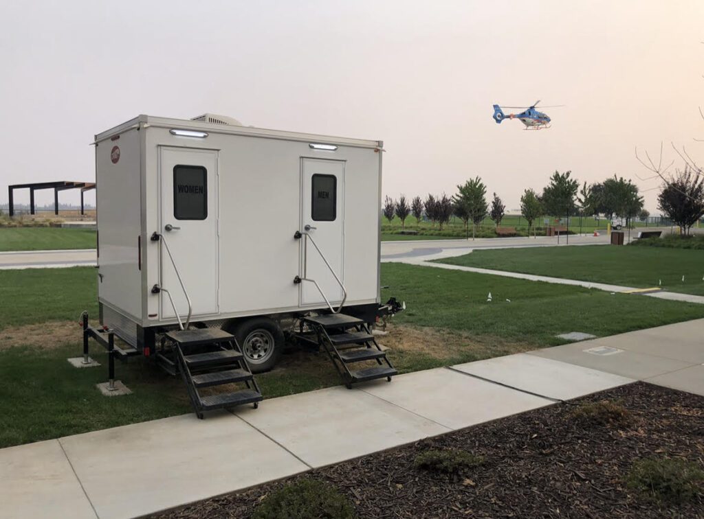 Bathroom trailer on a lawn under a hazy sky as a medical helicopter passes, The Lavatory Los Angeles