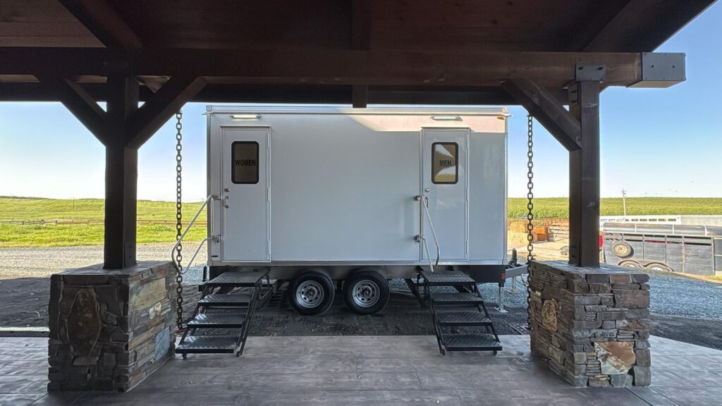 2-station bathroom trailer with women's and men's doors set under a timber and stone ranch pavilion, The Lavatory Los Angeles