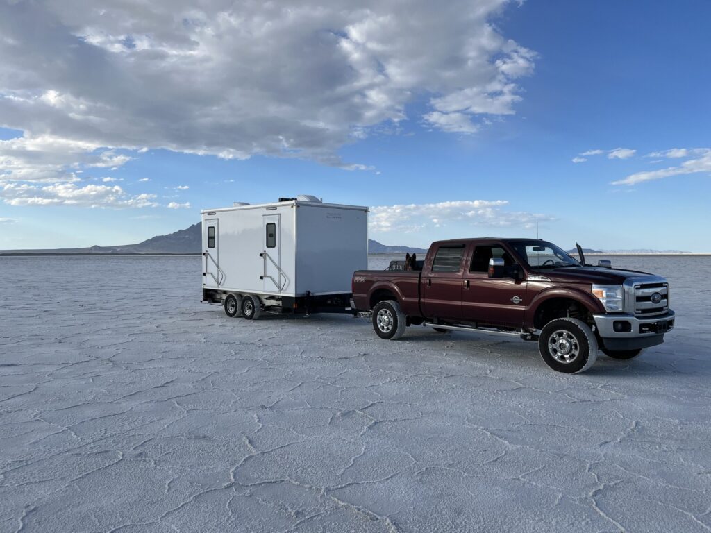 Luxury bathroom trailer towed by a pickup truck across open white salt flats, The Lavatory Los Angeles