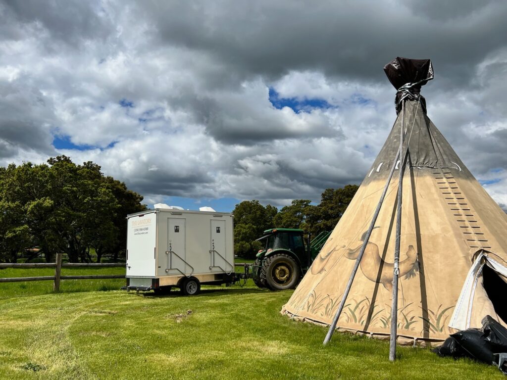 Bathroom trailer parked on a grassy ranch next to a large canvas tipi, The Lavatory Los Angeles