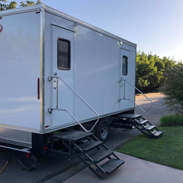 2-station bathroom trailer with women's and men's doors and steps beside a lawn, The Lavatory Los Angeles