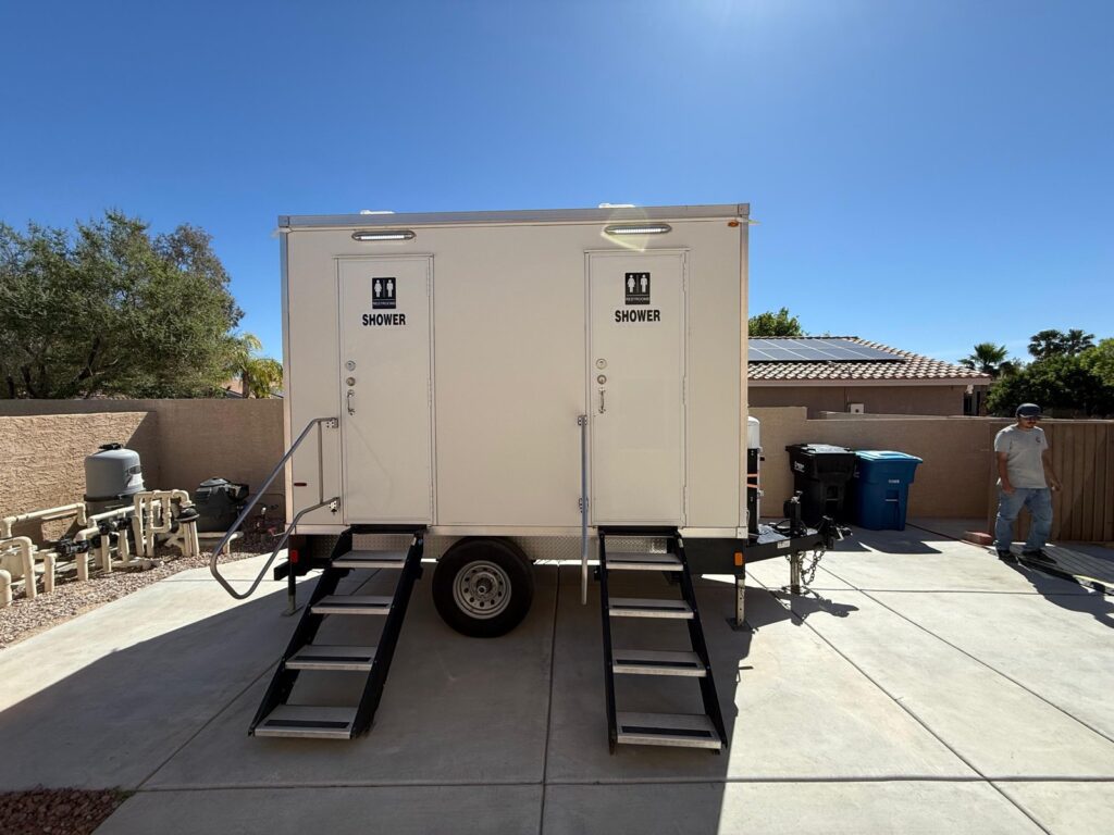 2-station combo shower trailer with two sets of steps on a backyard driveway as a worker from our team checks the setup, The Lavatory Los Angeles