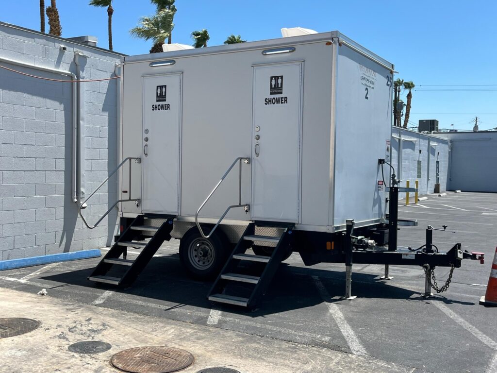 2-station combo trailer with two shower and bathroom doors and steps in a paved lot under palm trees, The Lavatory Los Angeles