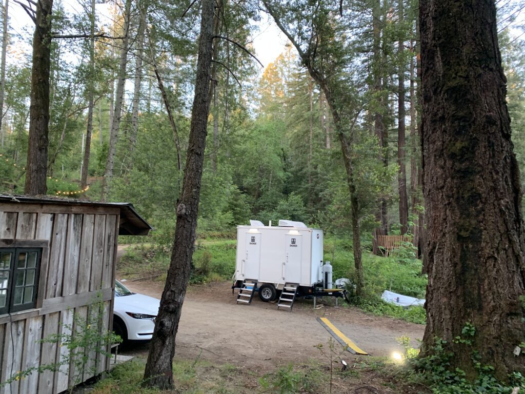 2-station private shower trailer parked in the woods near a rustic cabin, The Lavatory Los Angeles