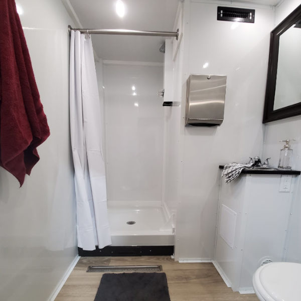 Shower stall with curtain, vanity and red towel inside a 2-station combo shower trailer room, The Lavatory Los Angeles