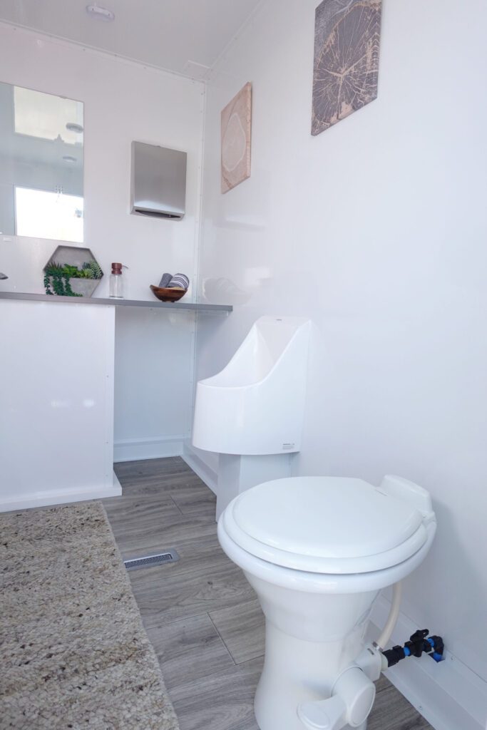 Men's room with a toilet, urinal and small vanity inside a 3-station private bathroom trailer, The Lavatory Los Angeles
