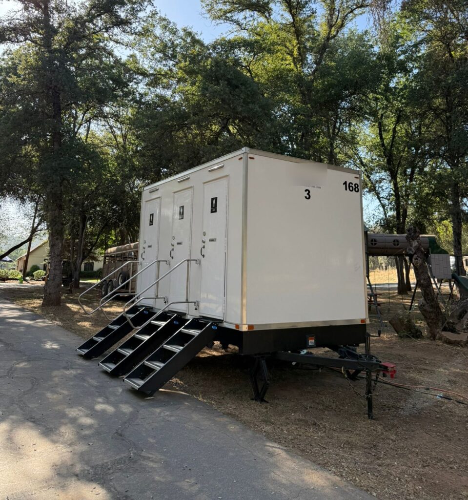 3-station bathroom trailer with three doors and fold-down steps set in a shady oak grove, The Lavatory Los Angeles