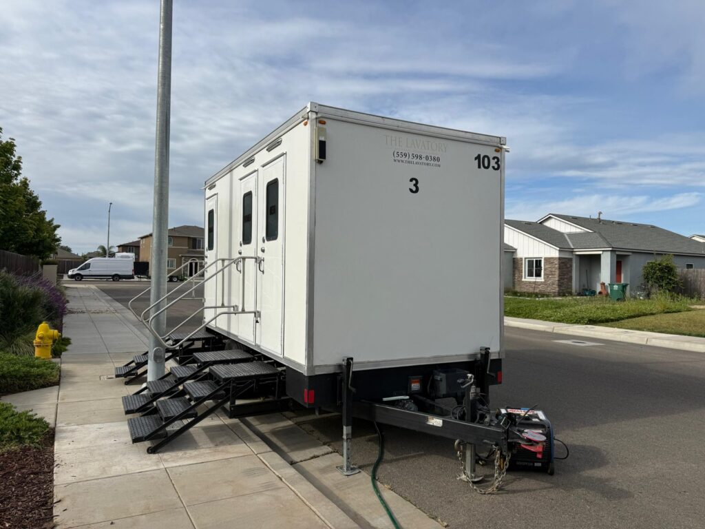 3-station mobile bathroom trailer parked at the curb on a residential street with its steps on the sidewalk, The Lavatory Los Angeles