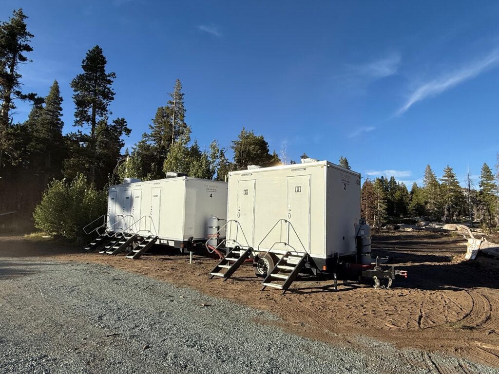 4-station combo trailer and 2-station combo trailer side by side on a dirt pad at a mountain forest camp, The Lavatory Los Angeles
