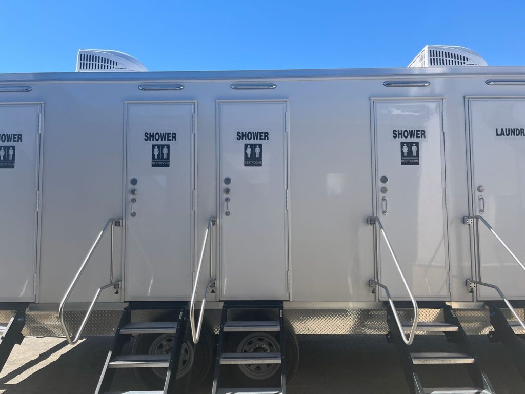 Row of private shower doors with restroom signs, handrails and stairs on a 4-station shower and laundry combo trailer, The Lavatory Los Angeles