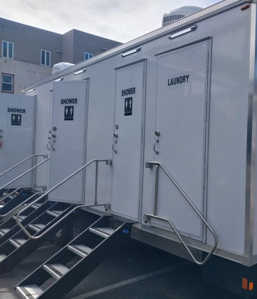 Close view of the shower and laundry doors with steel handrails and stairs on a 4-station combo trailer, The Lavatory Los Angeles