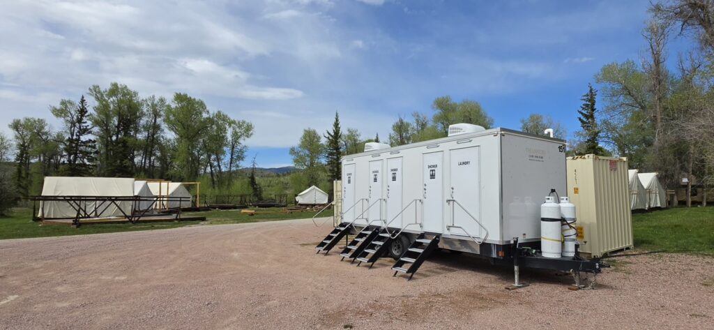 4-station combo trailer with propane tanks set on a gravel lot at a ranch youth summer camp with canvas tents, The Lavatory Los Angeles