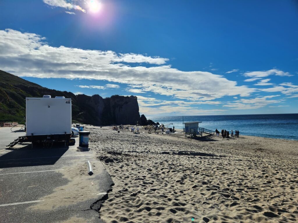 5-station bathroom trailer parked at the edge of a beach lot while event guests gather on the sand by the ocean, The Lavatory Los Angeles