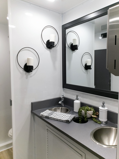 Double sink vanity with large mirror and ring wall sconces inside a 5-station bathroom trailer, The Lavatory Los Angeles