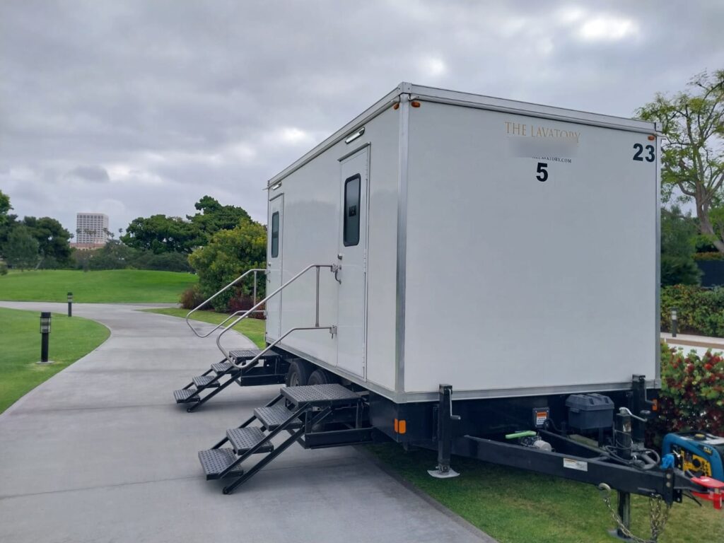5-station deluxe bathroom trailer with steps and handrails on a golf club cart path beside a green lawn, The Lavatory Los Angeles