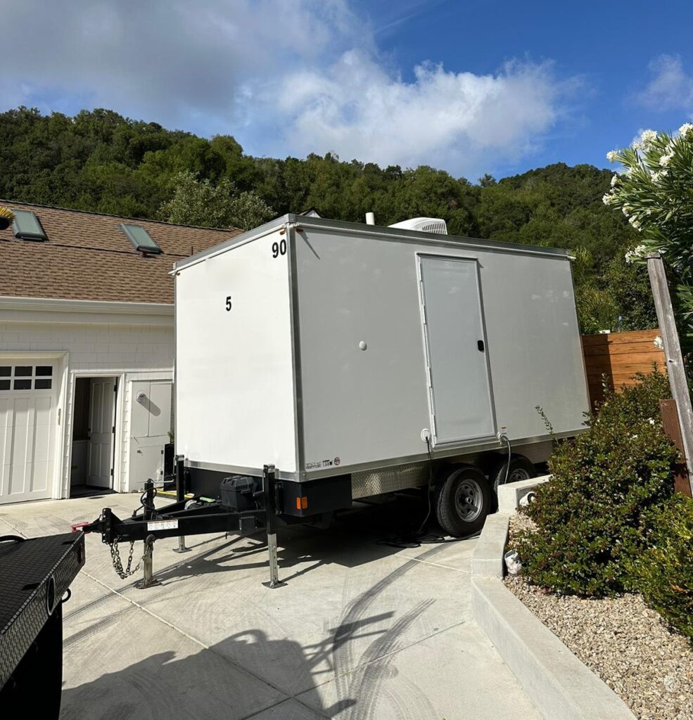 5-station bathroom trailer set in the driveway of a hillside home with wooded hills behind it, The Lavatory Los Angeles