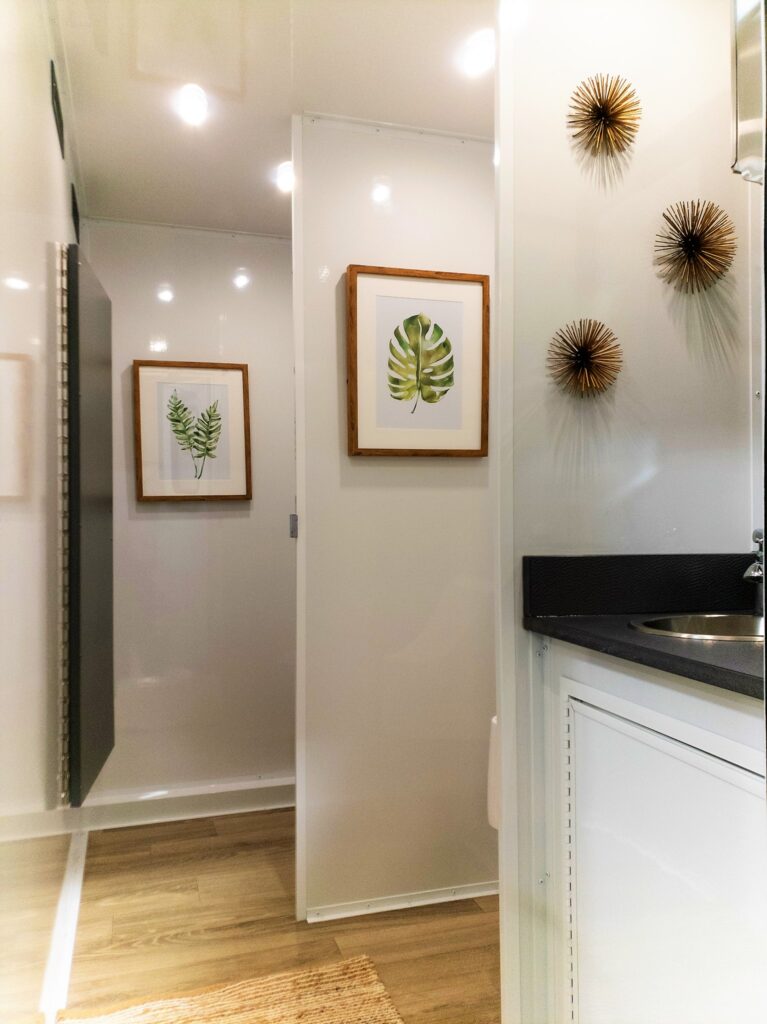 Men's room hallway with framed leaf art and sunburst decor inside a 5-station private bathroom trailer, The Lavatory Los Angeles