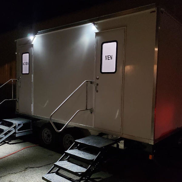 Luxury 5-station bathroom trailer lit up at night with women's and men's doors and entry steps, The Lavatory Los Angeles
