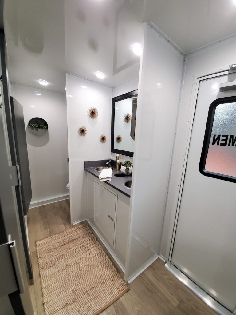 Women's room hallway with a vanity, framed mirror and wood-look floor inside a 5-station luxury bathroom trailer, The Lavatory Los Angeles