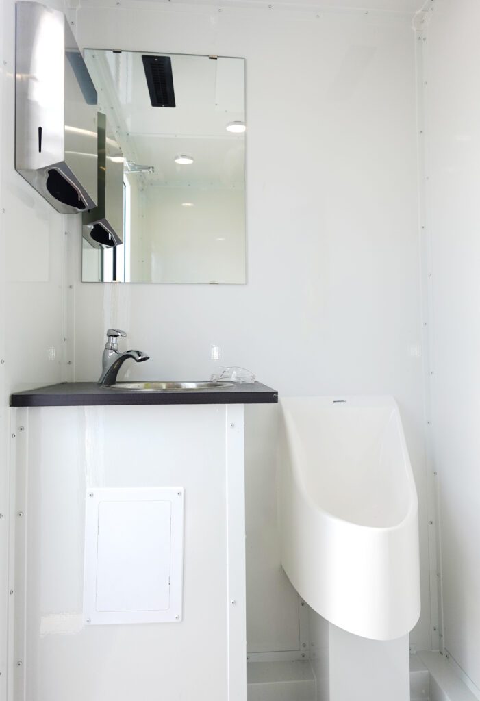 Compact private stall with a stainless sink, mirror, paper towel dispenser and urinal inside a deluxe bathroom trailer, The Lavatory Los Angeles