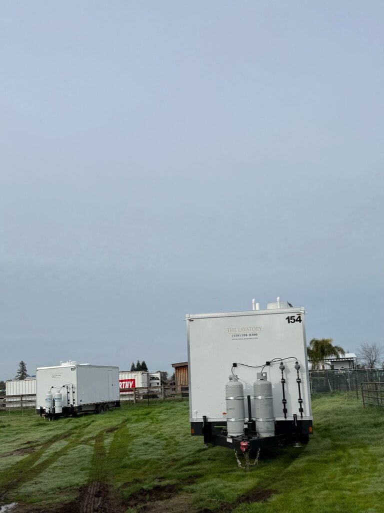 8-station laundry trailer with propane tanks parked on a grass field at a farm, The Lavatory Los Angeles