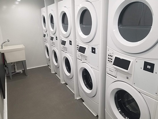 Stacked washers and dryers lined up beside a utility sink inside a mobile laundry trailer, The Lavatory Los Angeles