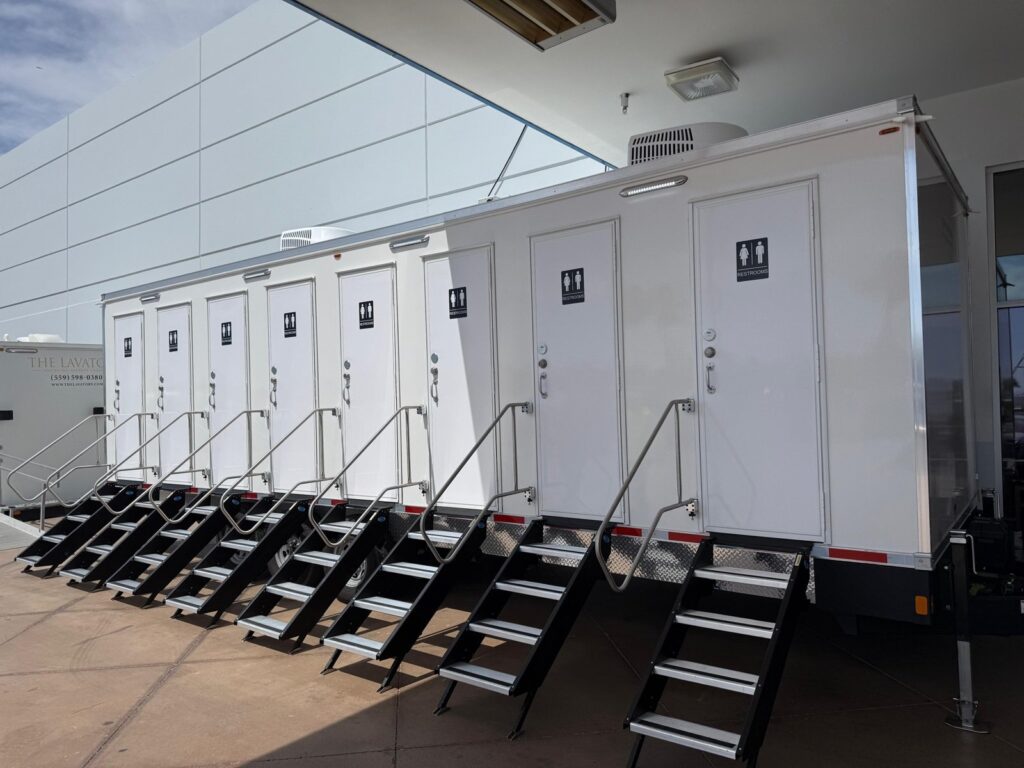 8-station private bathroom trailer with eight unisex doors and fold-down steps set up under a building canopy, The Lavatory Los Angeles