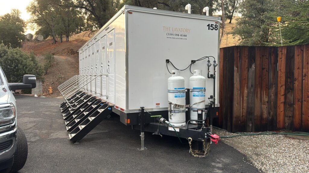 Rear corner of an 8-station private bathroom trailer showing the row of fold-down steps and side-mounted propane tanks, The Lavatory Los Angeles