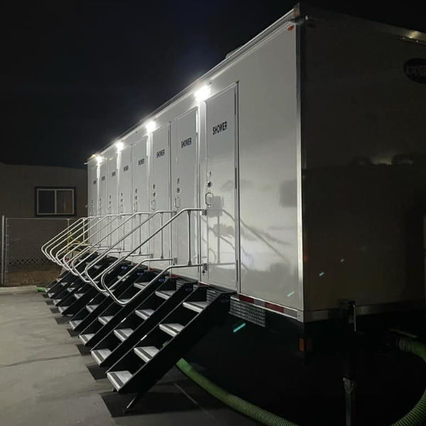 8-station private shower trailer lit up at night with steps at every door, The Lavatory Los Angeles