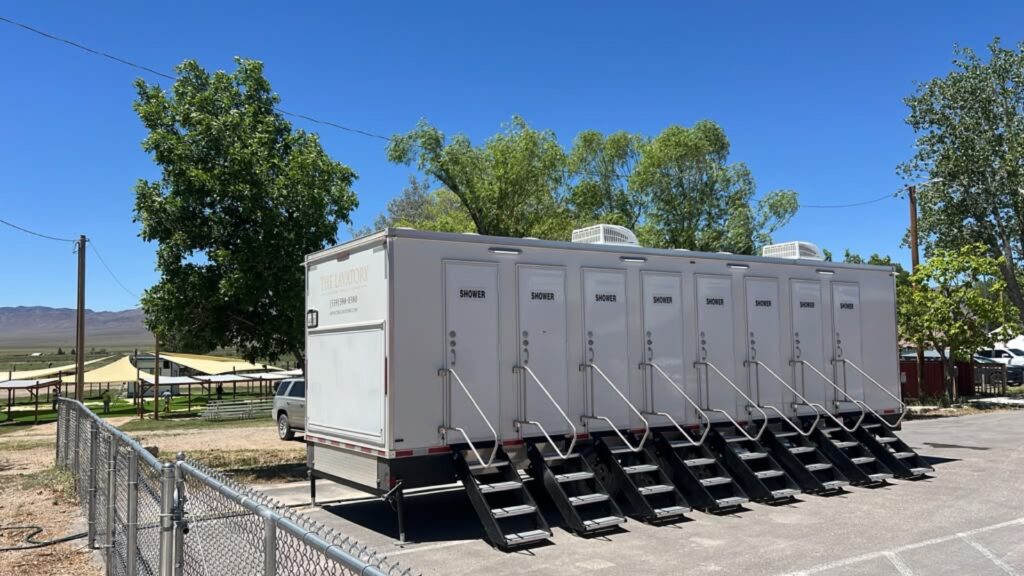 8-station shower trailer with steps at each door on a paved lot beside shade structures and desert hills, The Lavatory Los Angeles