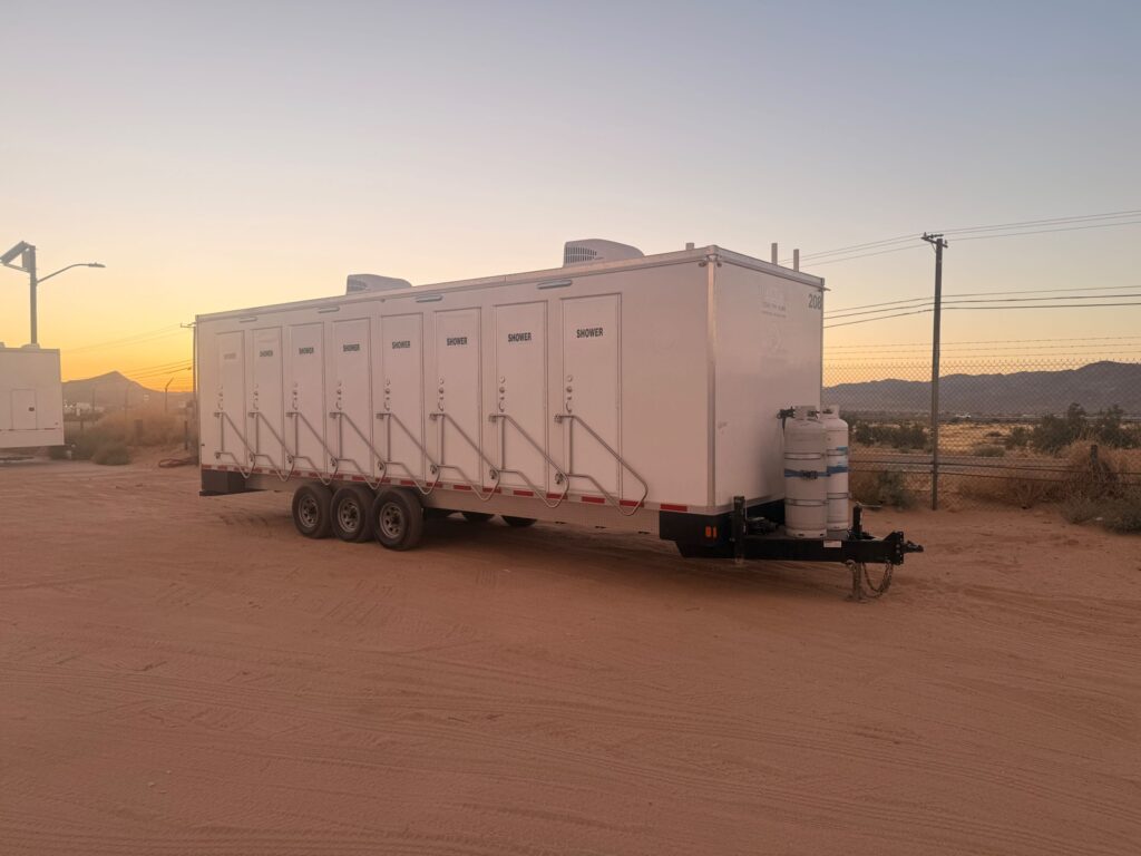 8-station shower trailer on a triple axle with propane tanks, parked on a desert lot at sunset, The Lavatory Los Angeles