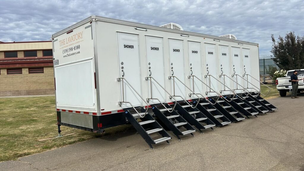8-station shower trailer with eight sets of steps on a campus path, with a staff member standing by a pickup truck, The Lavatory Los Angeles