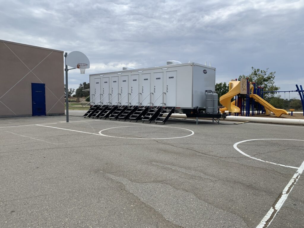 8-station shower trailer parked on a school basketball court beside a playground, The Lavatory Los Angeles