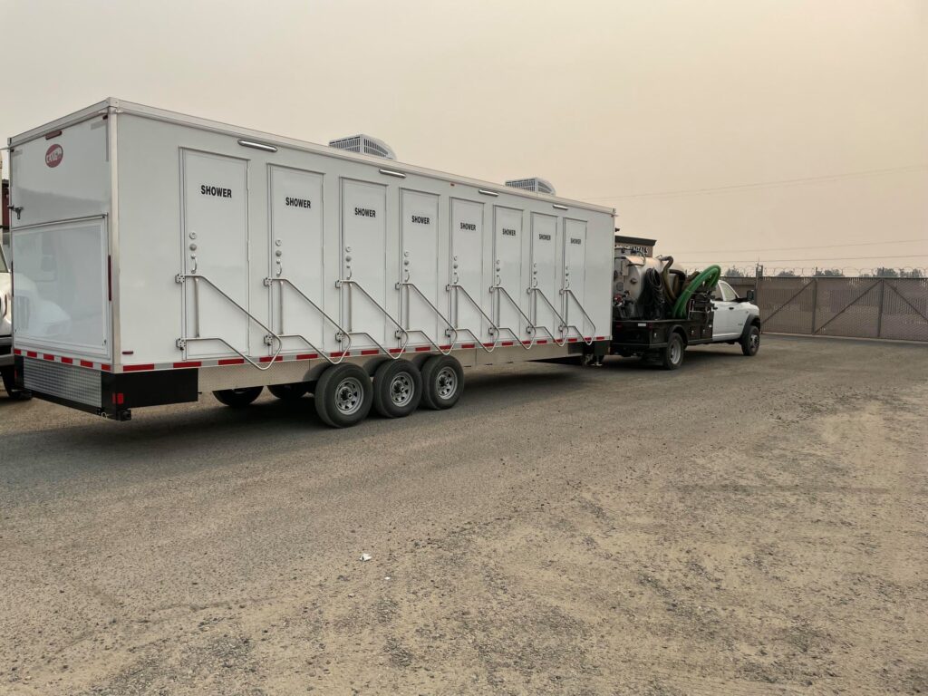 Hitched 8-station shower trailer on a gravel lot under a smoky orange sky during fire season, The Lavatory Los Angeles