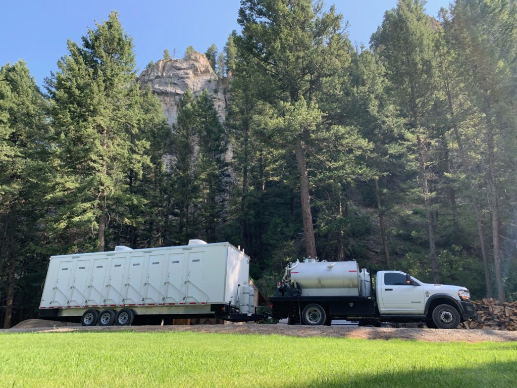 8-station shower trailer hitched to a water truck on grass beside a pine forest, The Lavatory Los Angeles