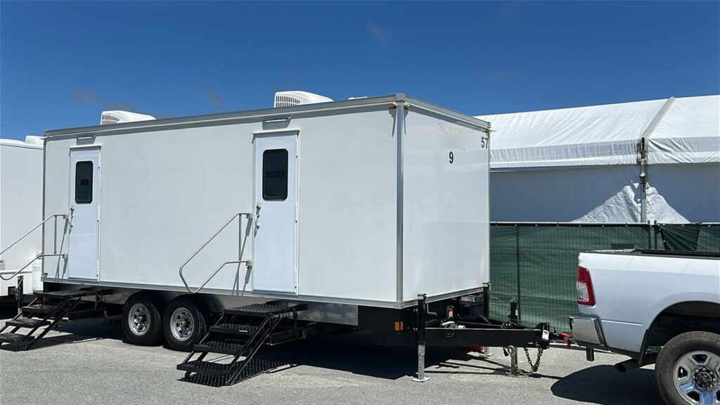 9-station luxury bathroom trailer with men's and women's entries and fold-down steps parked beside a large white event tent, The Lavatory Los Angeles