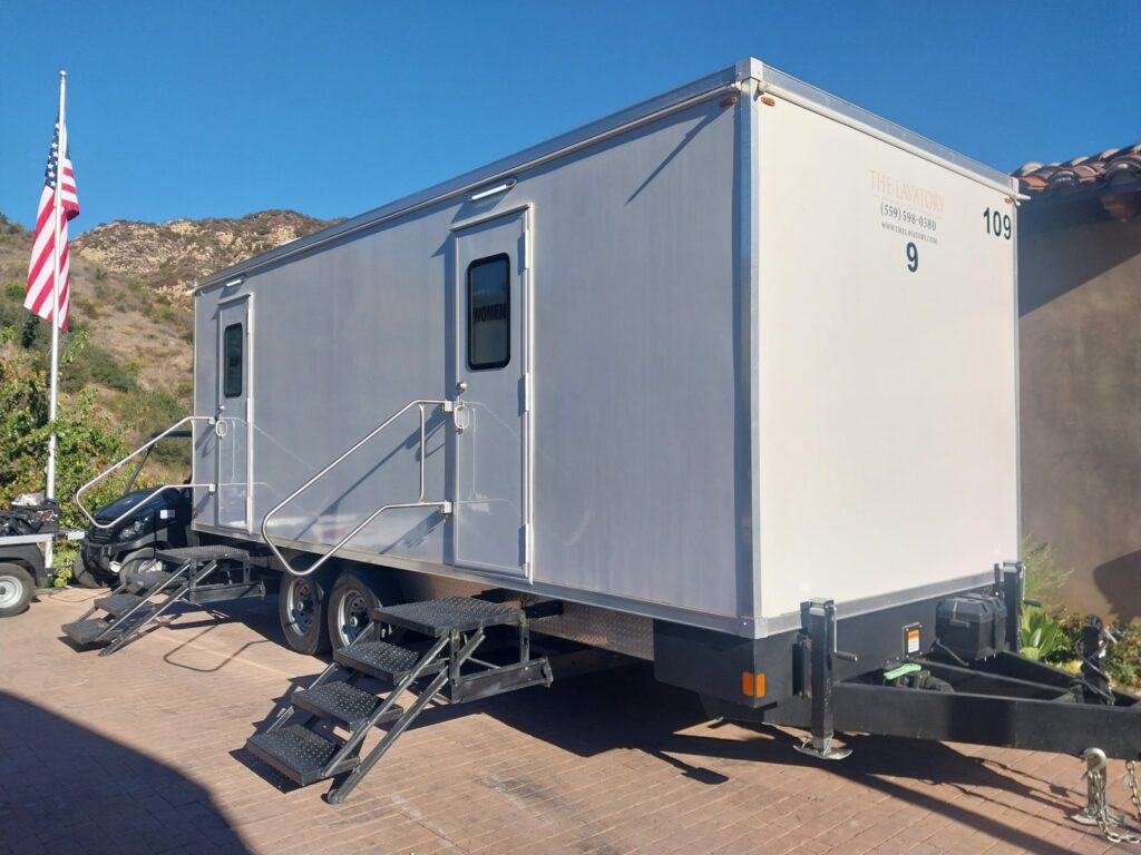 9-station luxury bathroom trailer on a brick driveway at a hillside estate beside a flag pole, The Lavatory Los Angeles