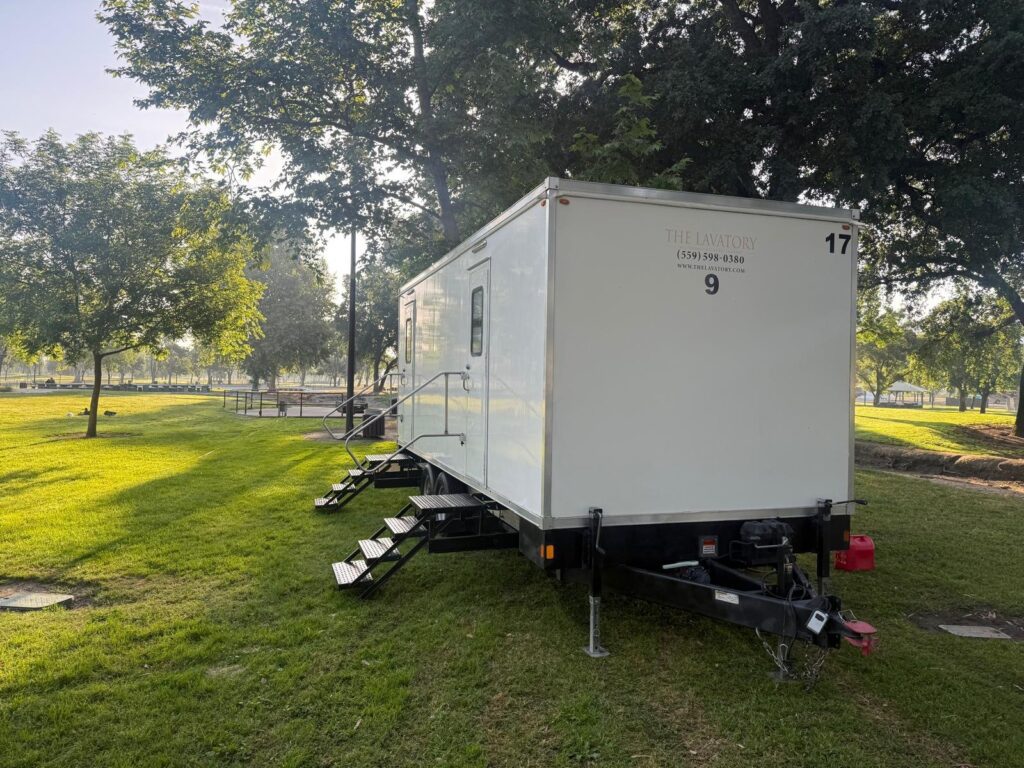 9-station mobile bathroom trailer on a park lawn under shade trees in morning light, The Lavatory Los Angeles