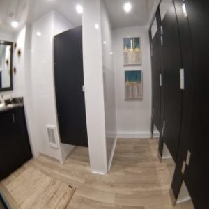 Row of dark stall partitions and a wood-look floor on the women's side of a 9-station luxury bathroom trailer, The Lavatory Los Angeles