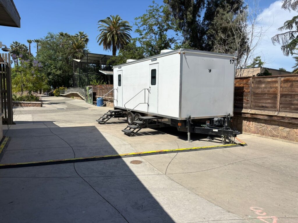 9-station bathroom trailer set on a paved visitor path under palm trees during a public water outage, The Lavatory Los Angeles