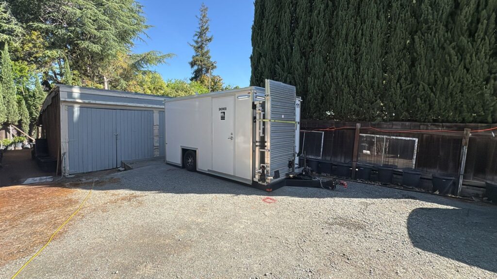 Accessible combo trailer parked on a gravel driveway beside a garage in a private backyard, The Lavatory Los Angeles
