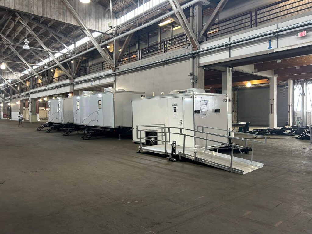 Accessible combo trailer with its ramp beside two bathroom trailers inside a pier hall for an indoor summit, The Lavatory Los Angeles