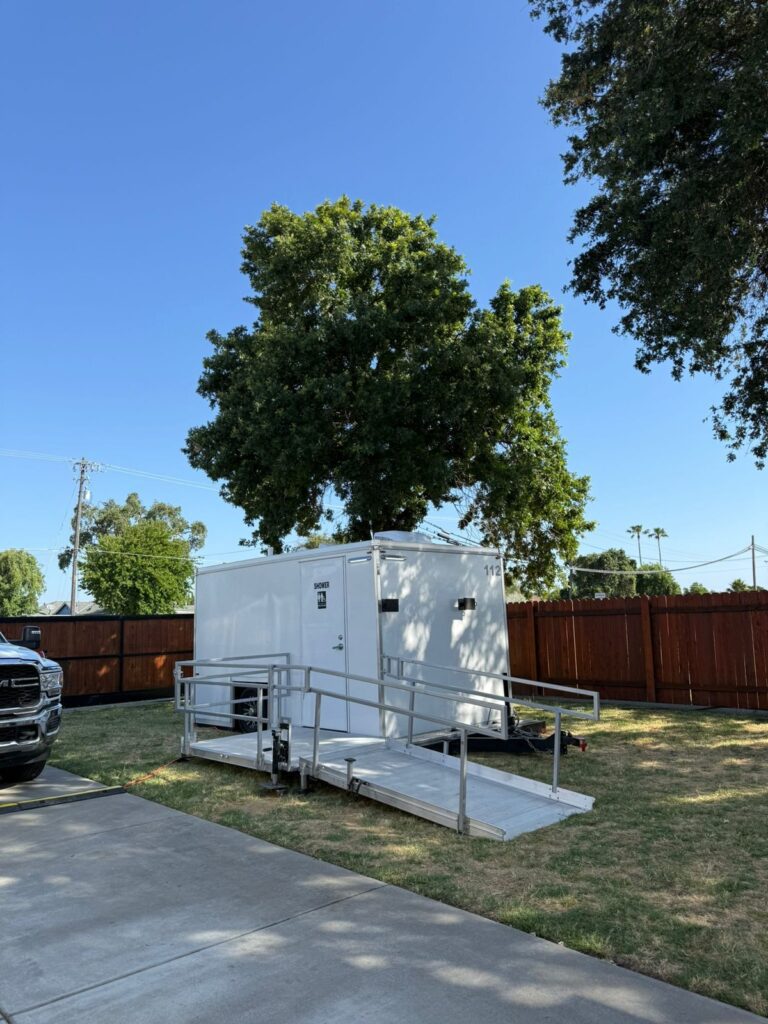 Accessible combo trailer with a ramp on a lawn beside a driveway and a wood fence for a fire department, The Lavatory Los Angeles