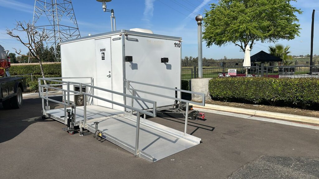 Accessible combo shower and bathroom trailer with a railed ramp and landing set up by our team on a paved event lot, The Lavatory Los Angeles