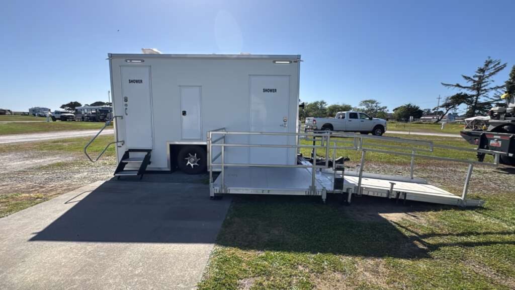 ADA plus 2 shower trailer with entry steps and a long aluminum ramp on a grassy field near the coast, The Lavatory Los Angeles